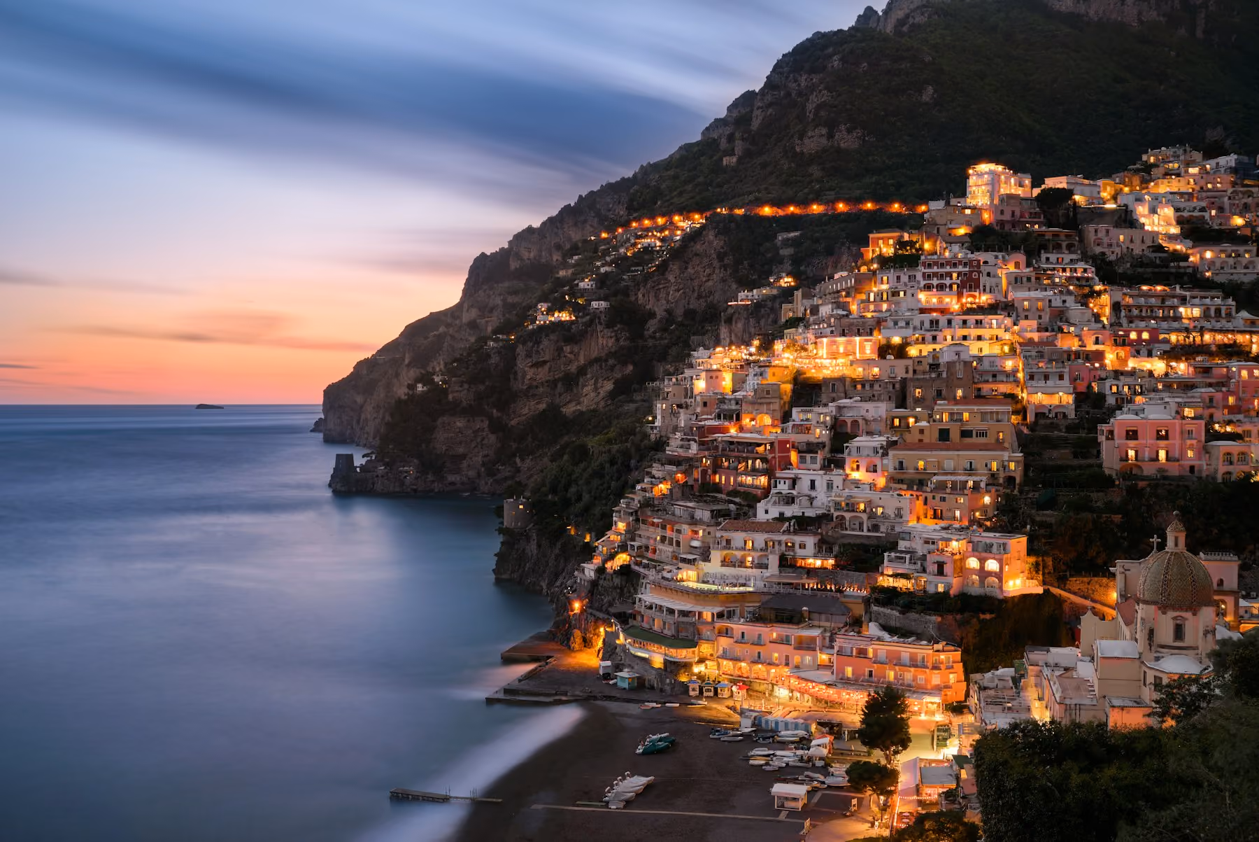 Positano lit up at dusk above a calm sea
