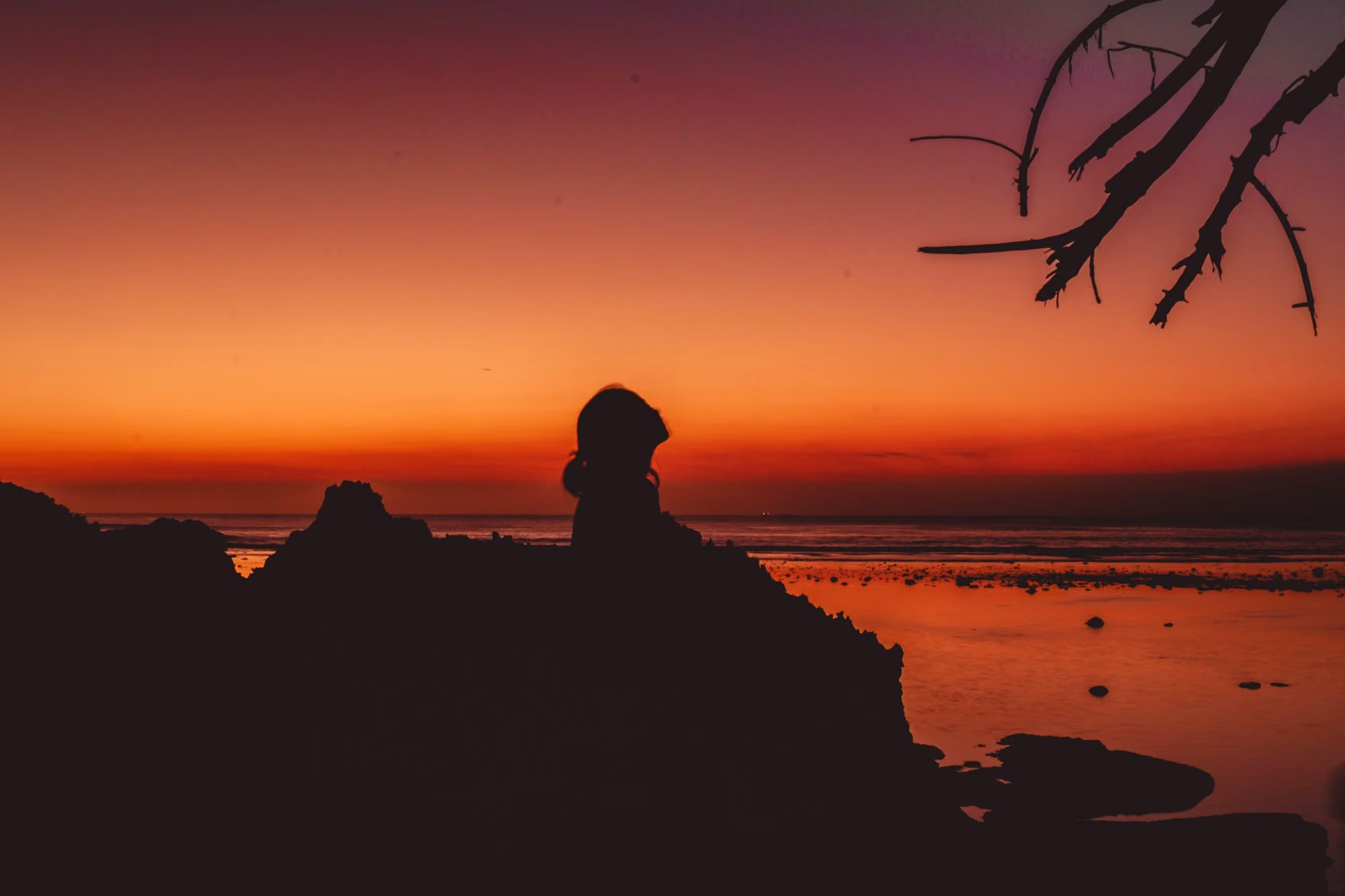 Near Jimbaran Puri, A Belmond Hotel: a silhouette of a person sitting on a rock at sunset