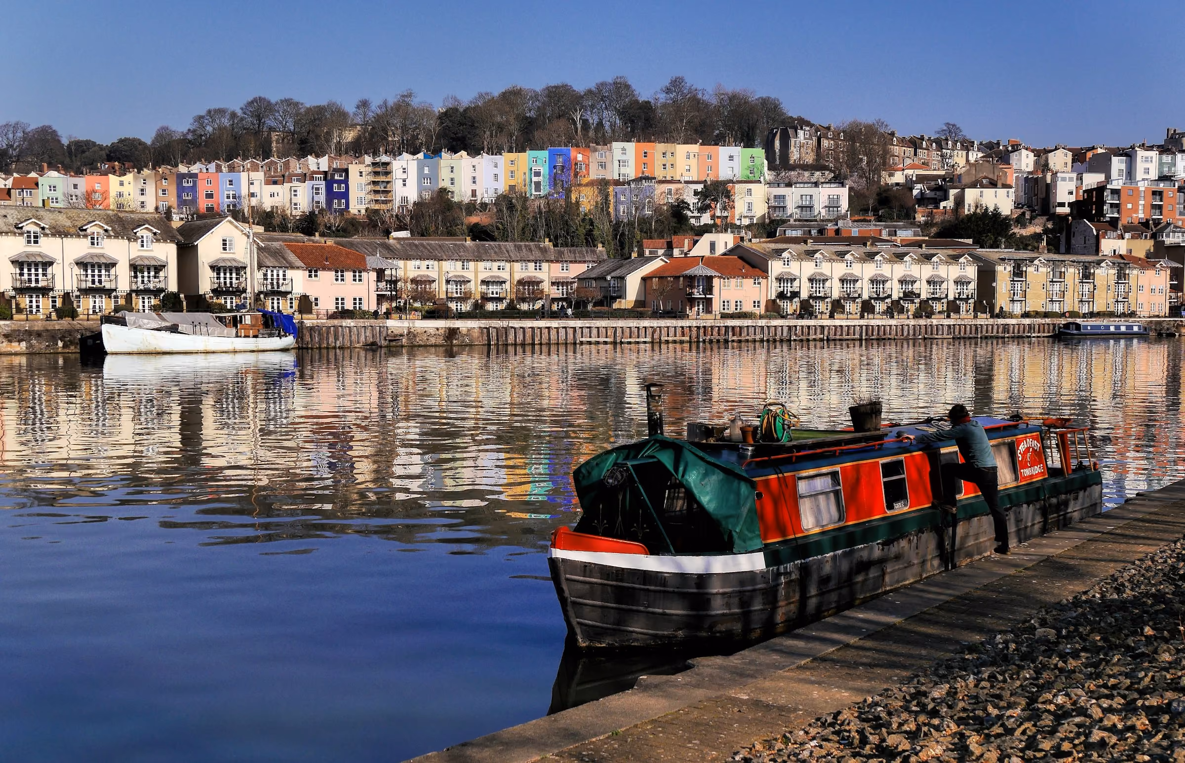 A narrowboat in Bristol's harbour below coloured houses