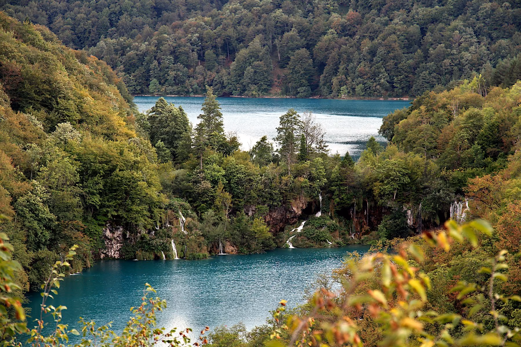 Lakes and waterfalls at Plitvice framed by forest, with leaves beginning to turn