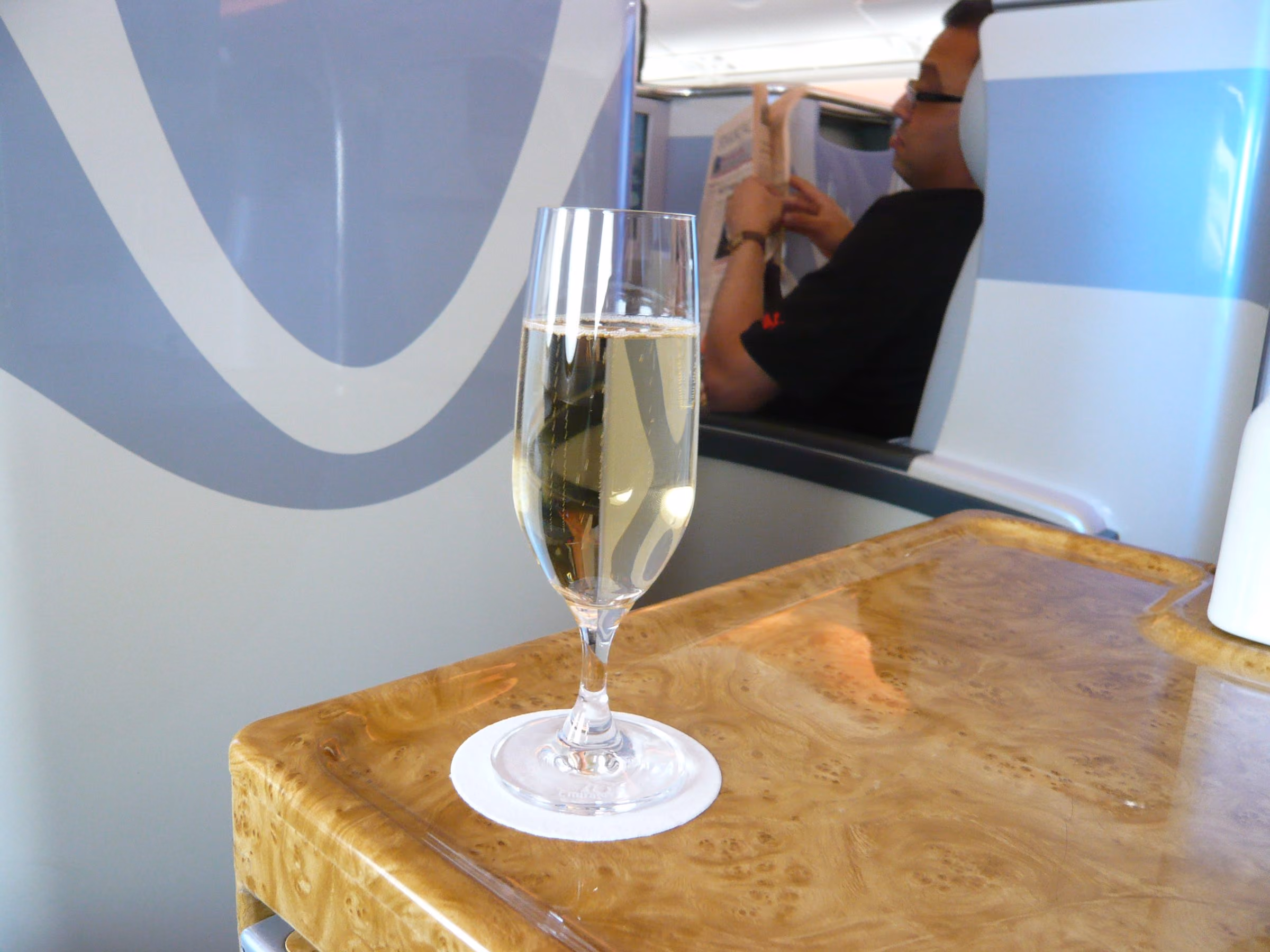 A glass of champagne on the walnut side table of an Emirates A380 business class seat