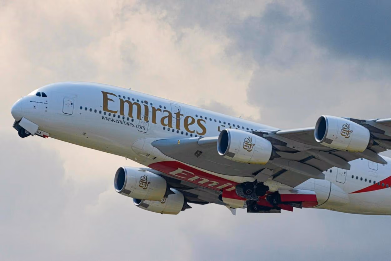 An Emirates A380 climbing out against a stormy sky, gear still down