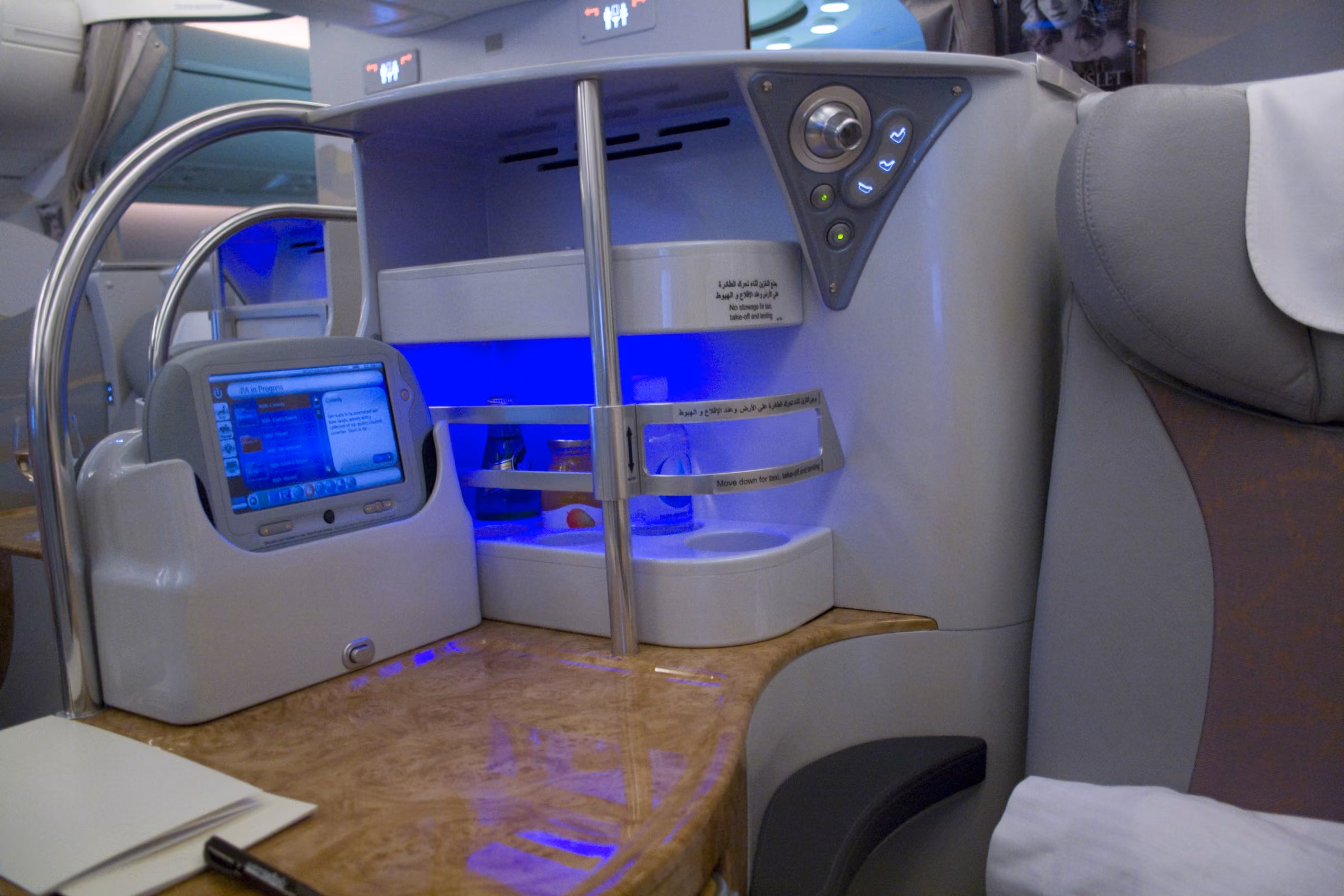 The handset, screen controls and lit minibar beside an Emirates A380 business class seat