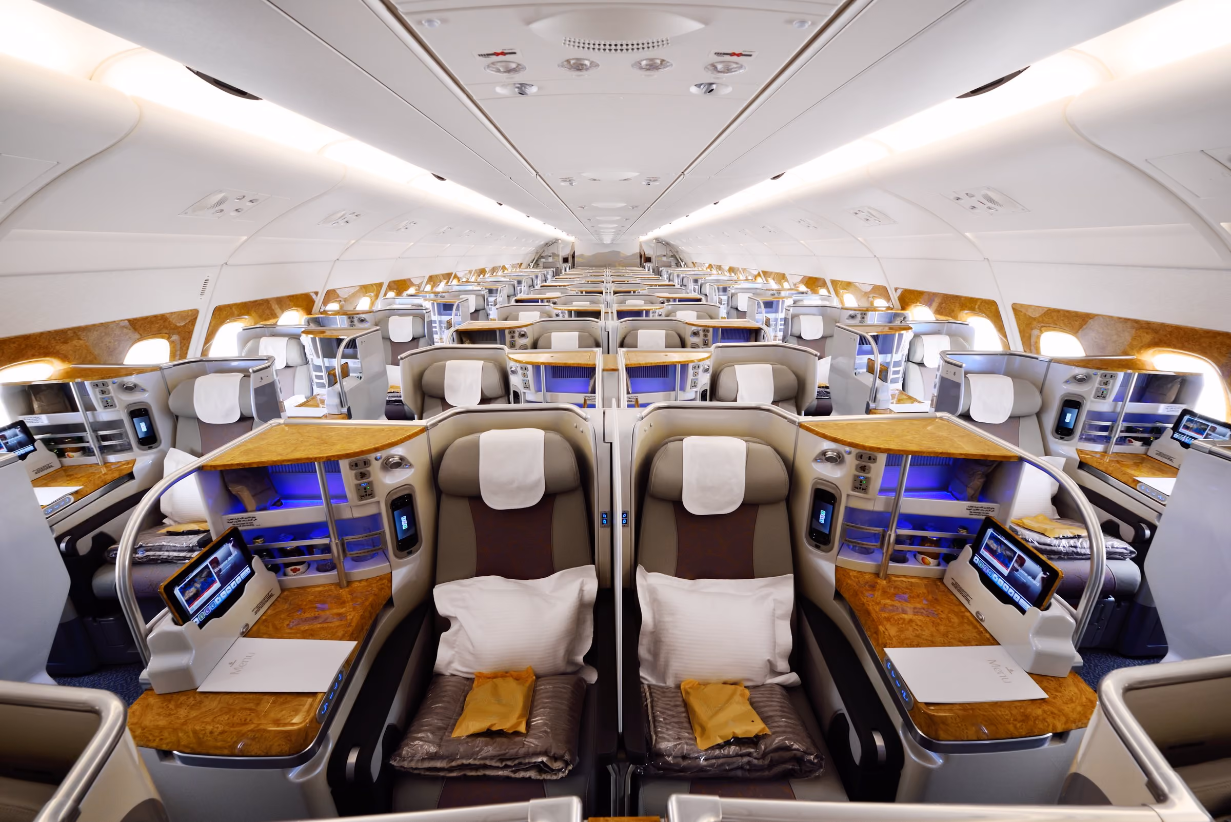 A centre pair of Emirates A380 business class seats made up with pillows and blankets under low cabin light