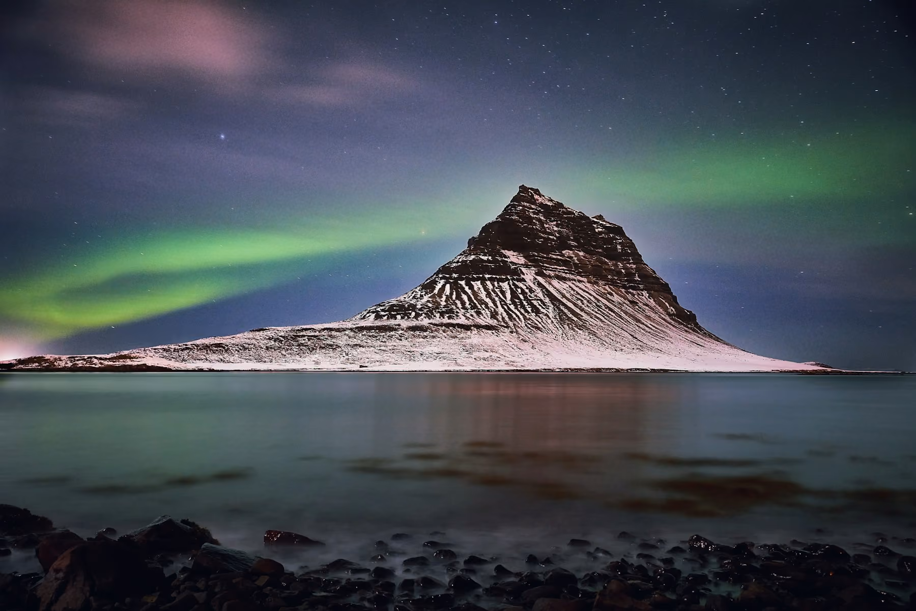 Green northern lights over snow-covered Kirkjufell mountain, the best time to visit Iceland for aurora