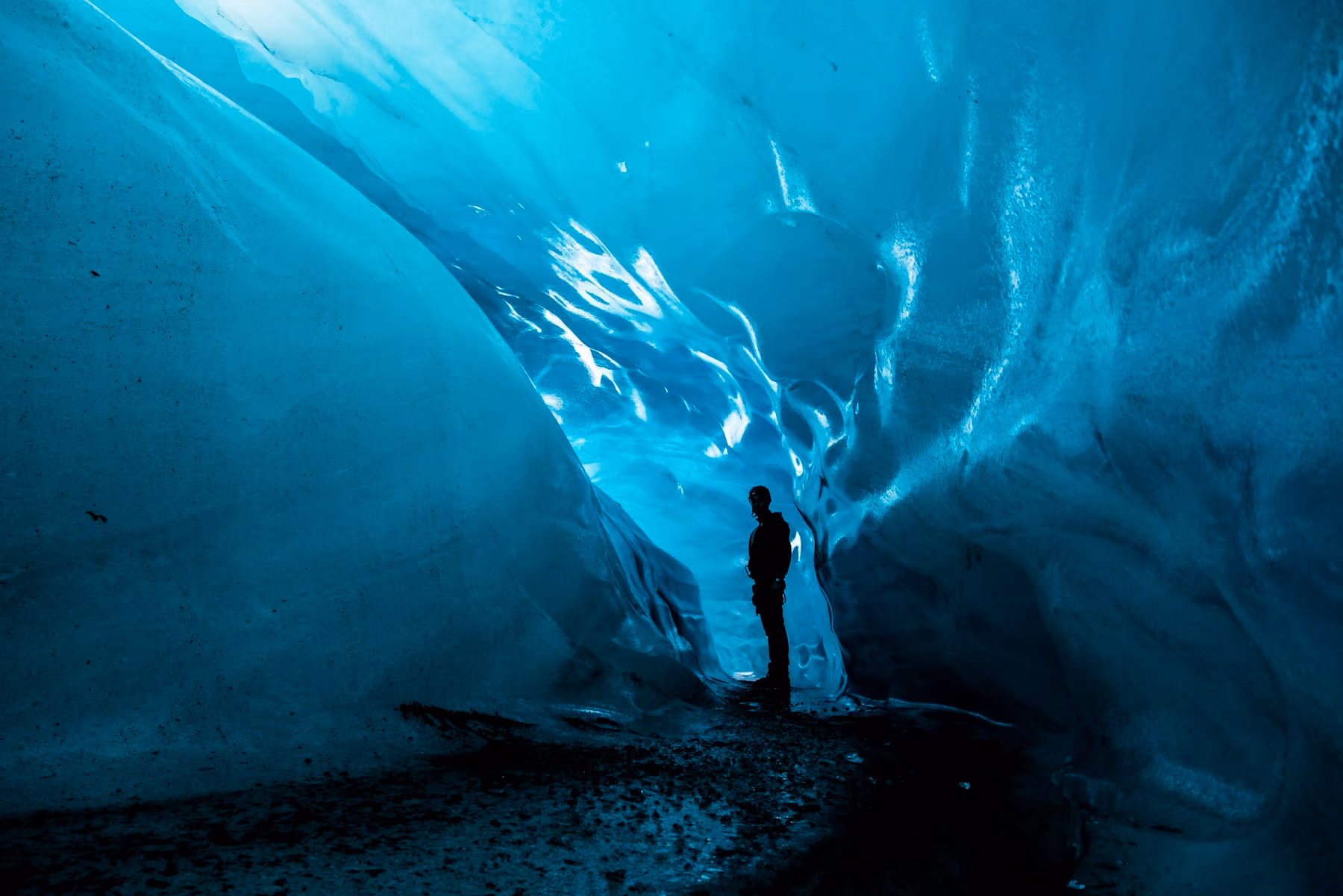 A lone figure inside a glowing blue ice cave beneath the Vatnajökull glacier