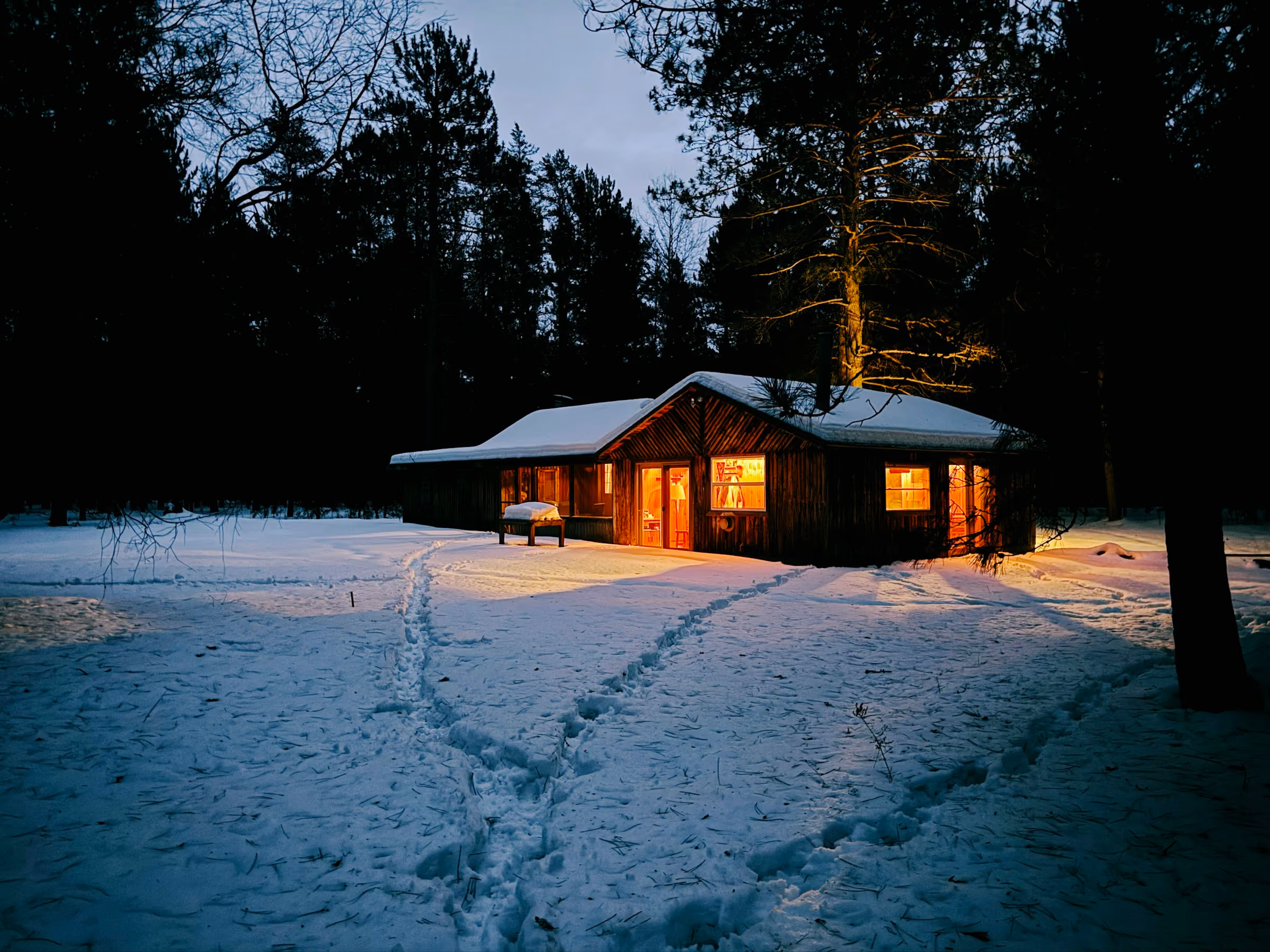 Footprints across the snow to a lit wooden lodge at night