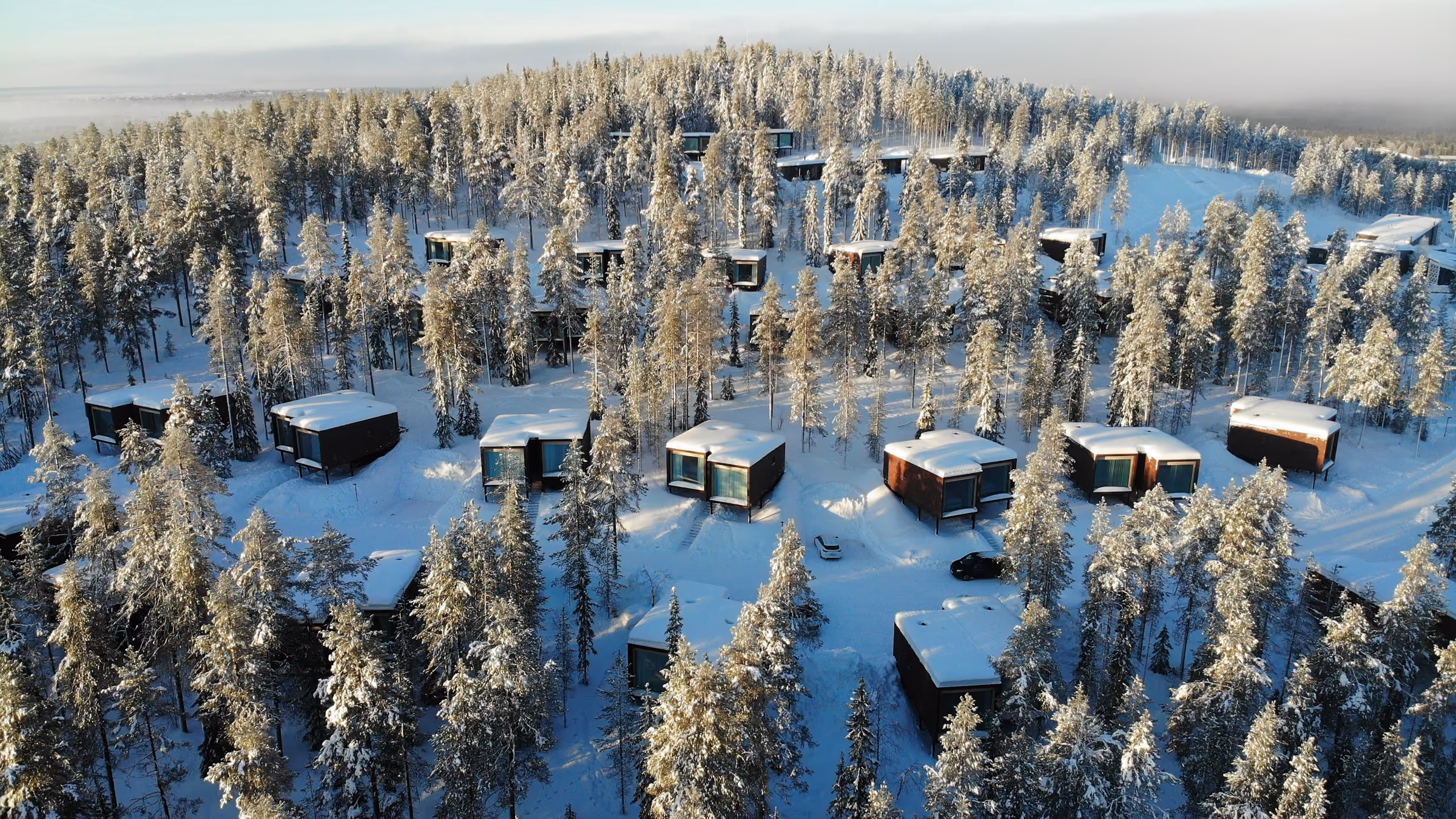 Cabins scattered through a snowy forest seen from above