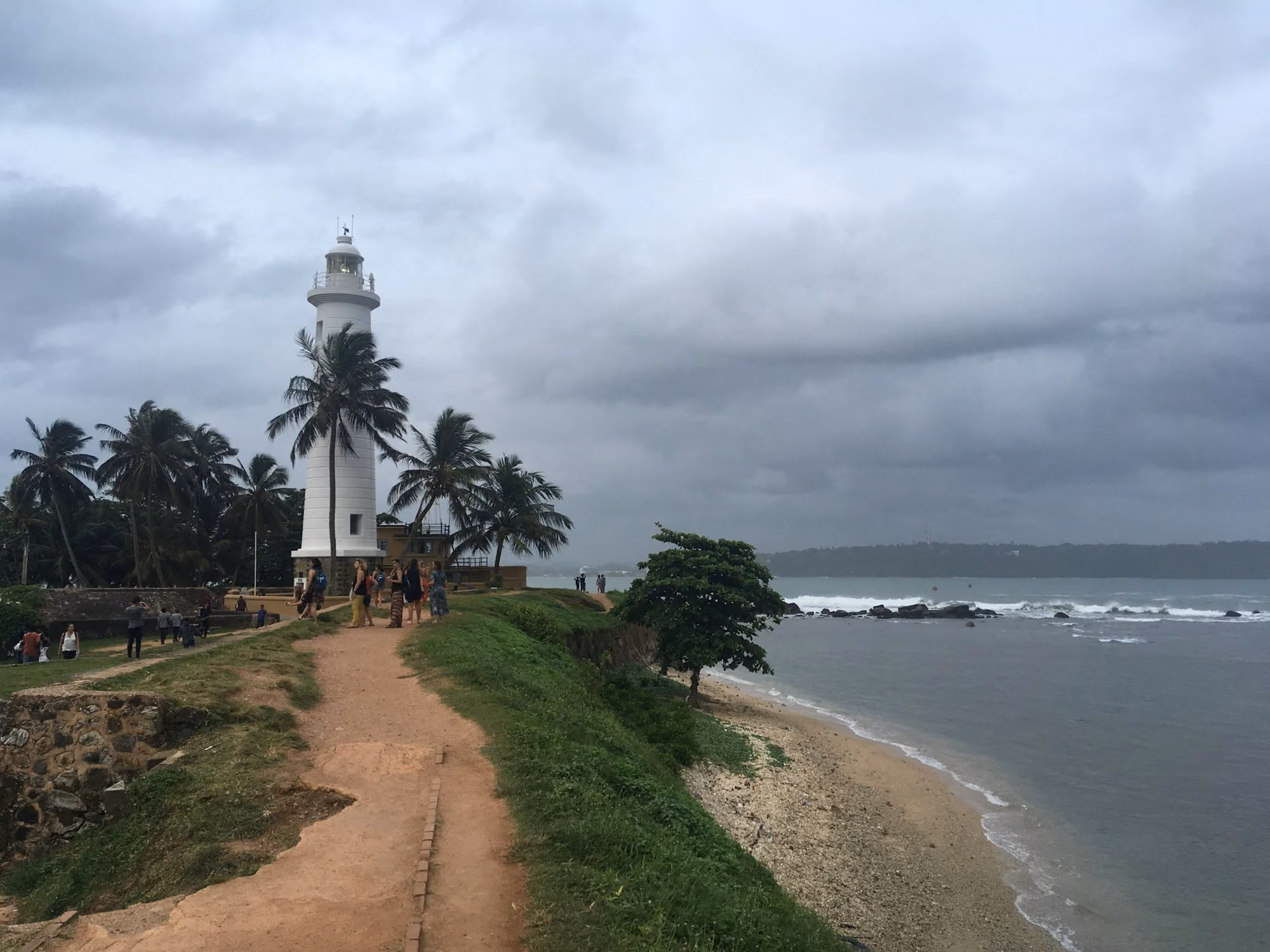 Near Amangalla: White lighthouse on a coastal path with palm trees