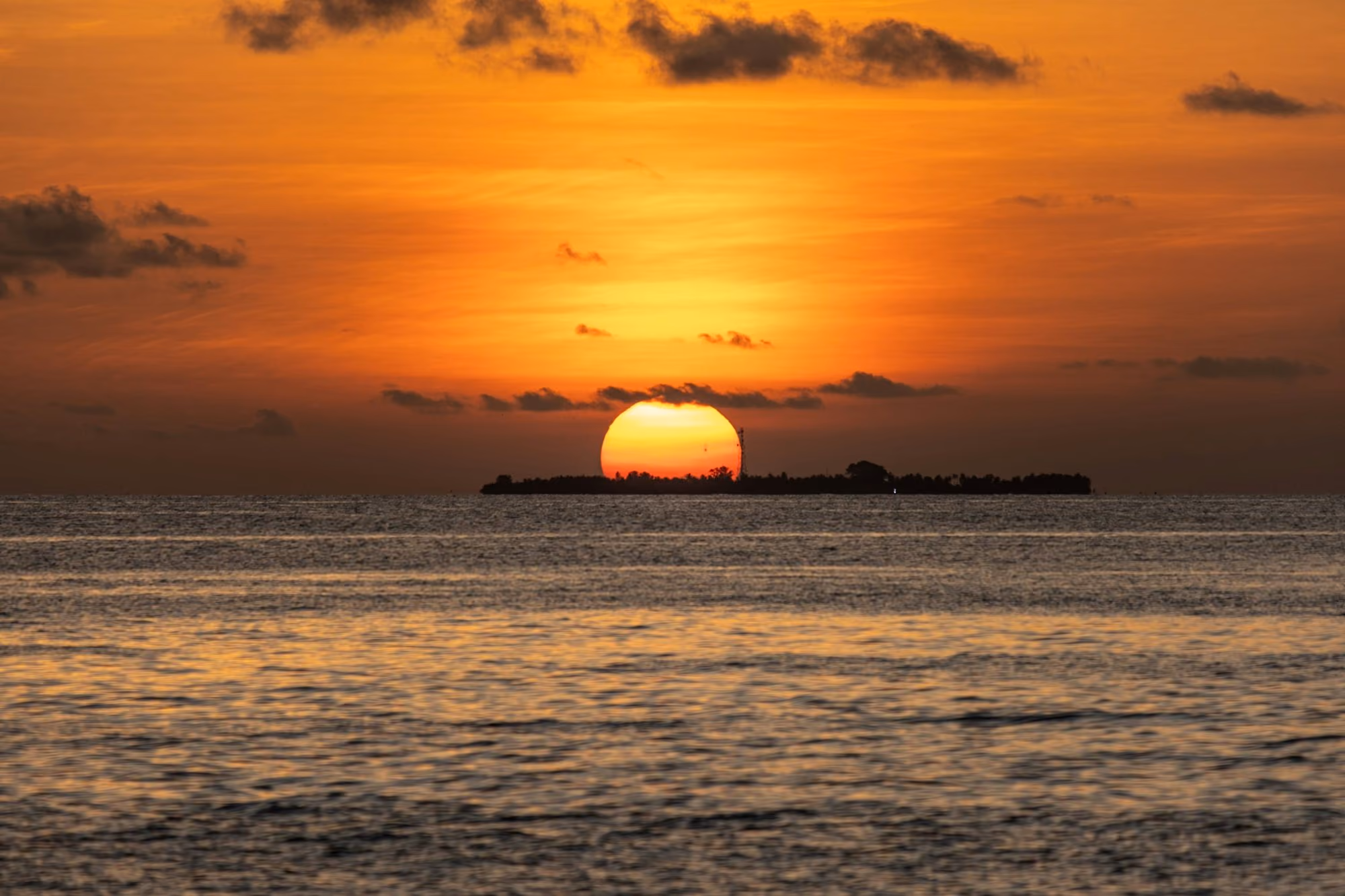 Near Soneva Jani: the sun is setting over the ocean with a small island in the distance