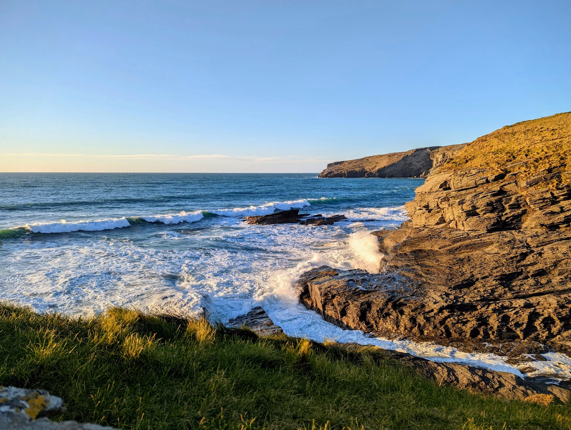 Surf breaking below Cornish cliffs at sunset