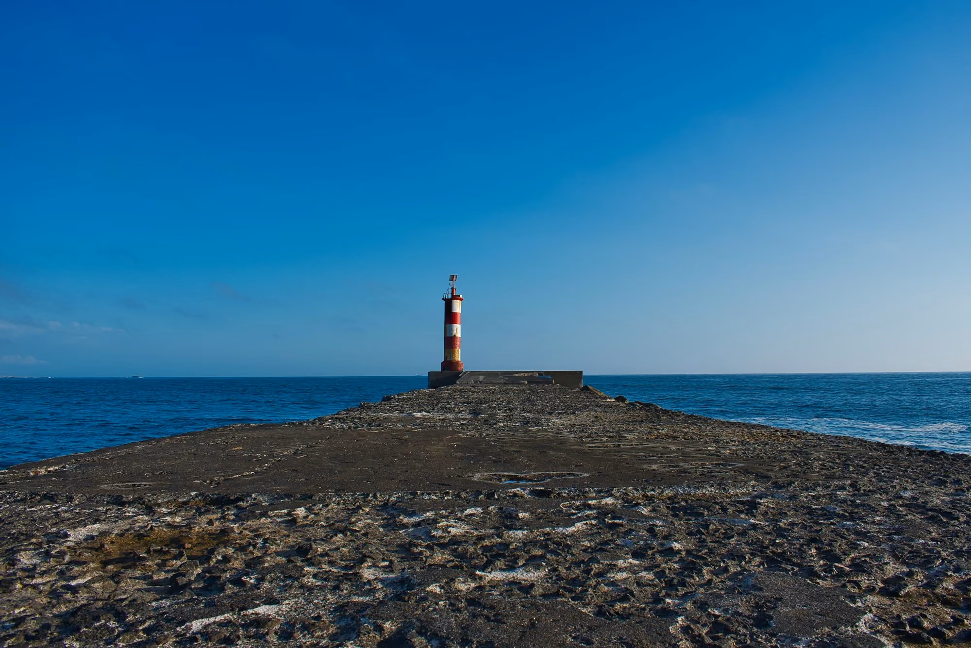 Near The Lince Santa Clara: red and white lighthouse on brown rocky shore under blue sky during daytime