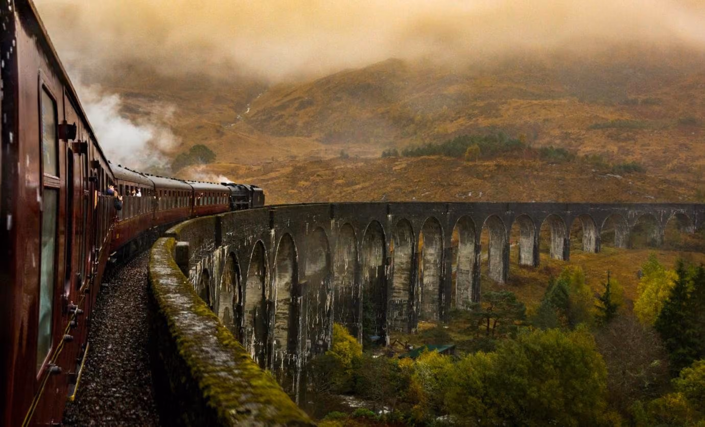 A train on a curving stone viaduct in the Highlands, autumn mist on the hills