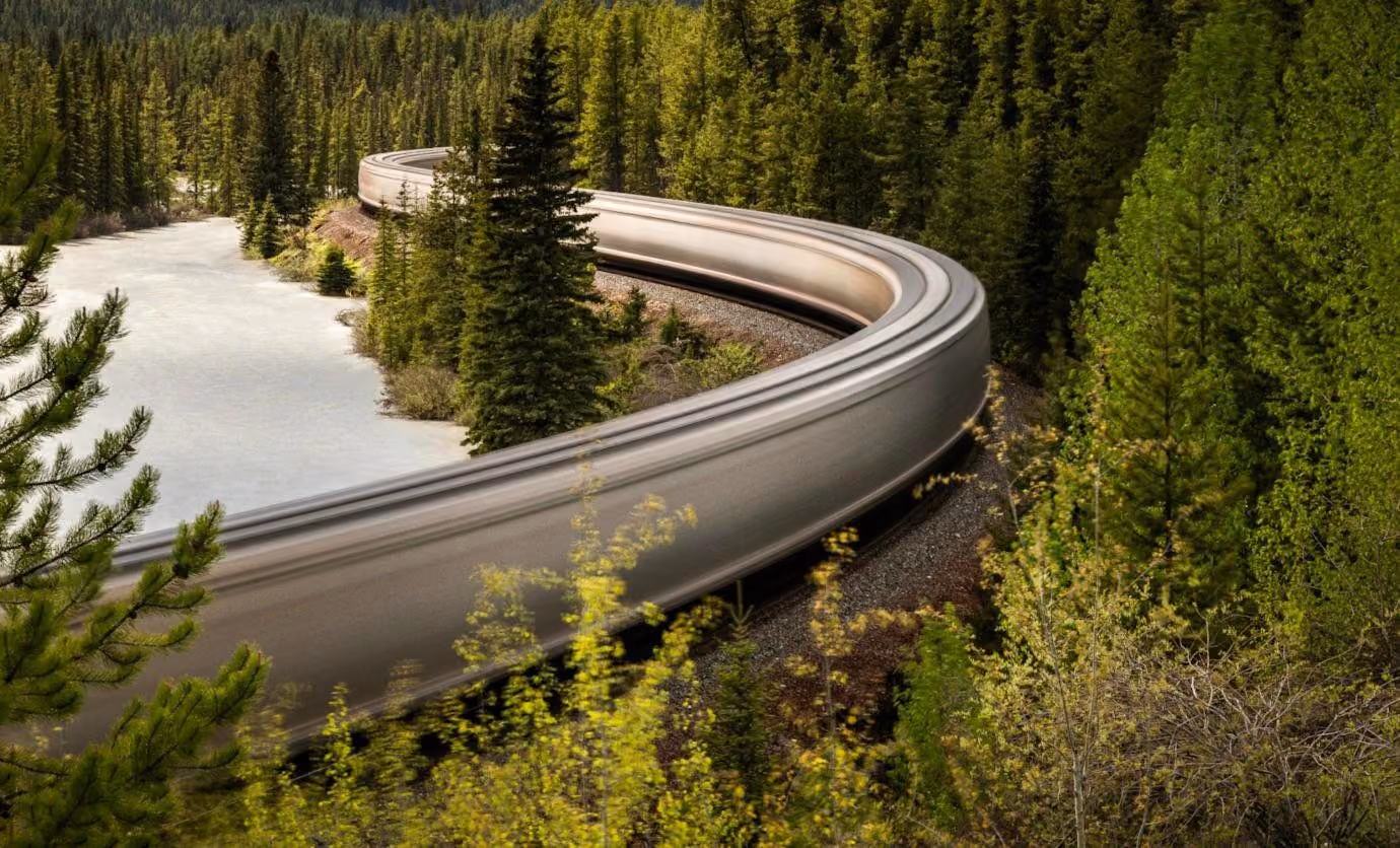 A train blurs round a curve through pine forest beside a frozen river