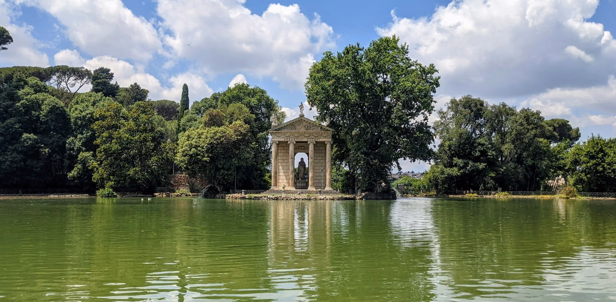 Near Hotel Eden, Dorchester Collection: a lake with a gazebo surrounded by trees