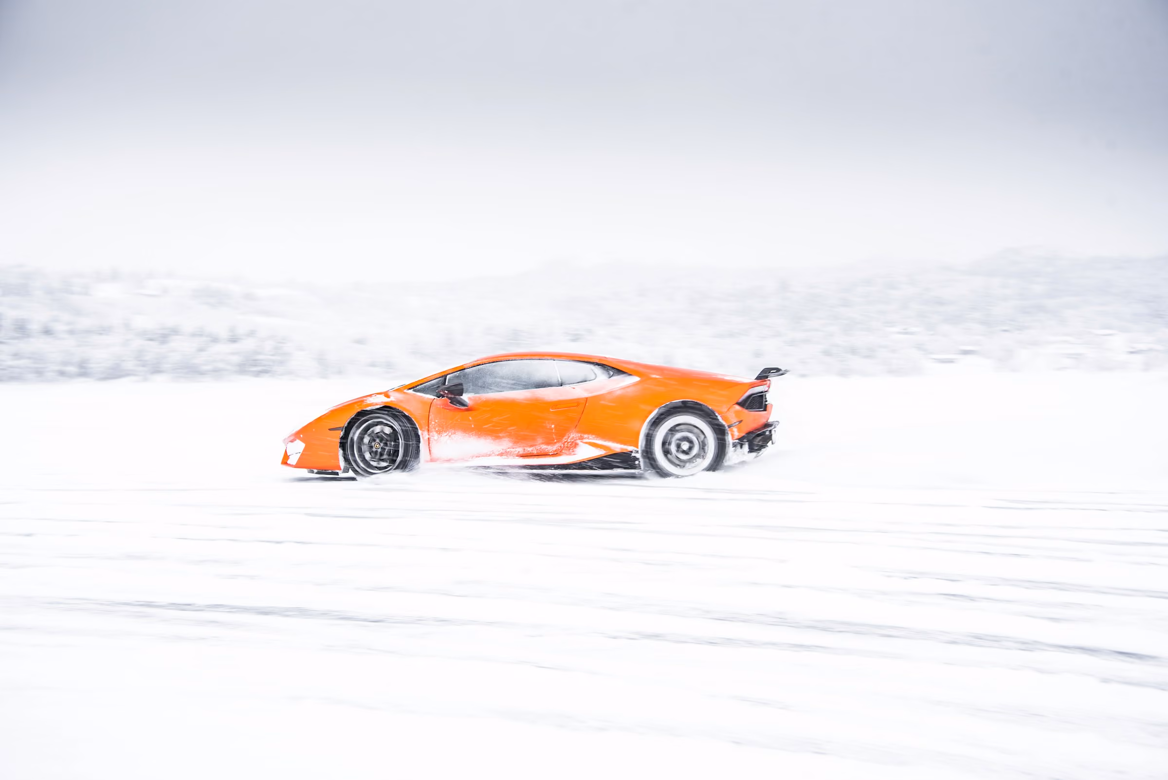 An orange supercar driving across a snowfield
