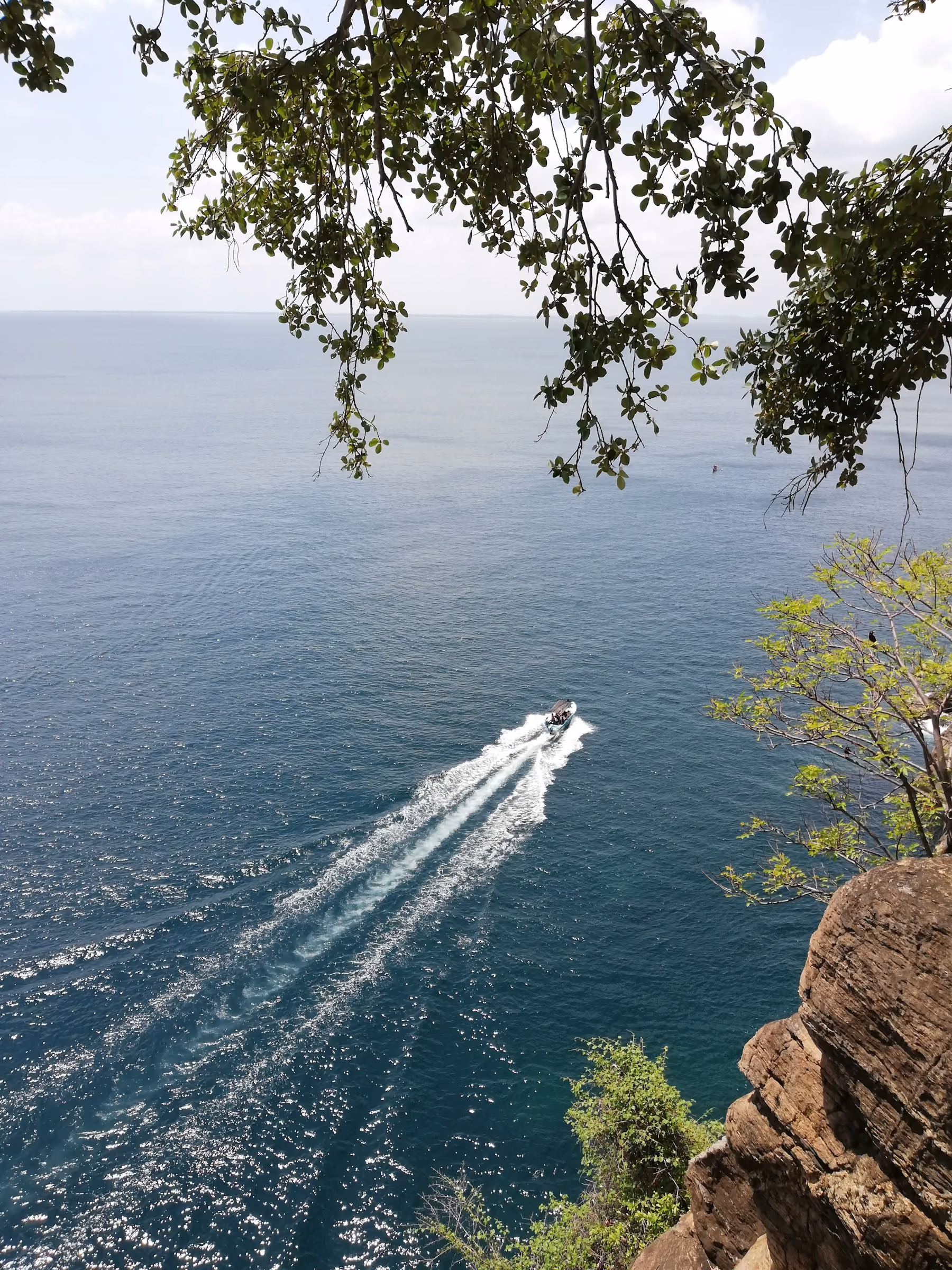 A speedboat cutting across calm blue water below the cliffs at Trincomalee