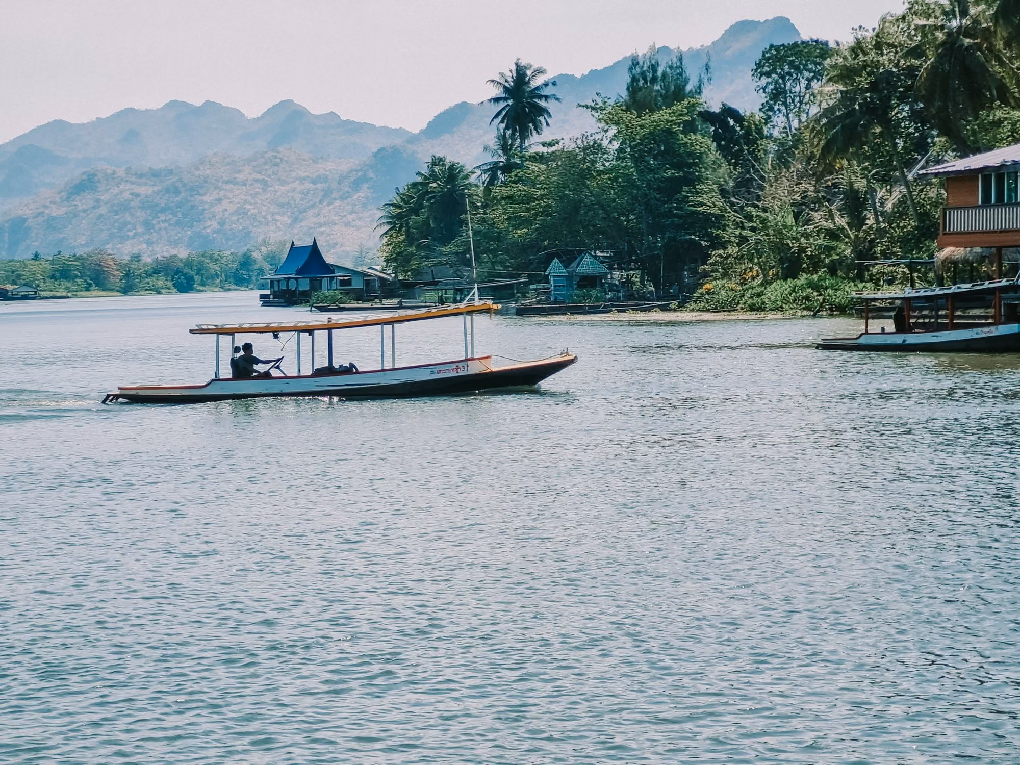 Near Anantara Golden Triangle Elephant Camp & Resort: a boat traveling down a river next to a lush green hillside