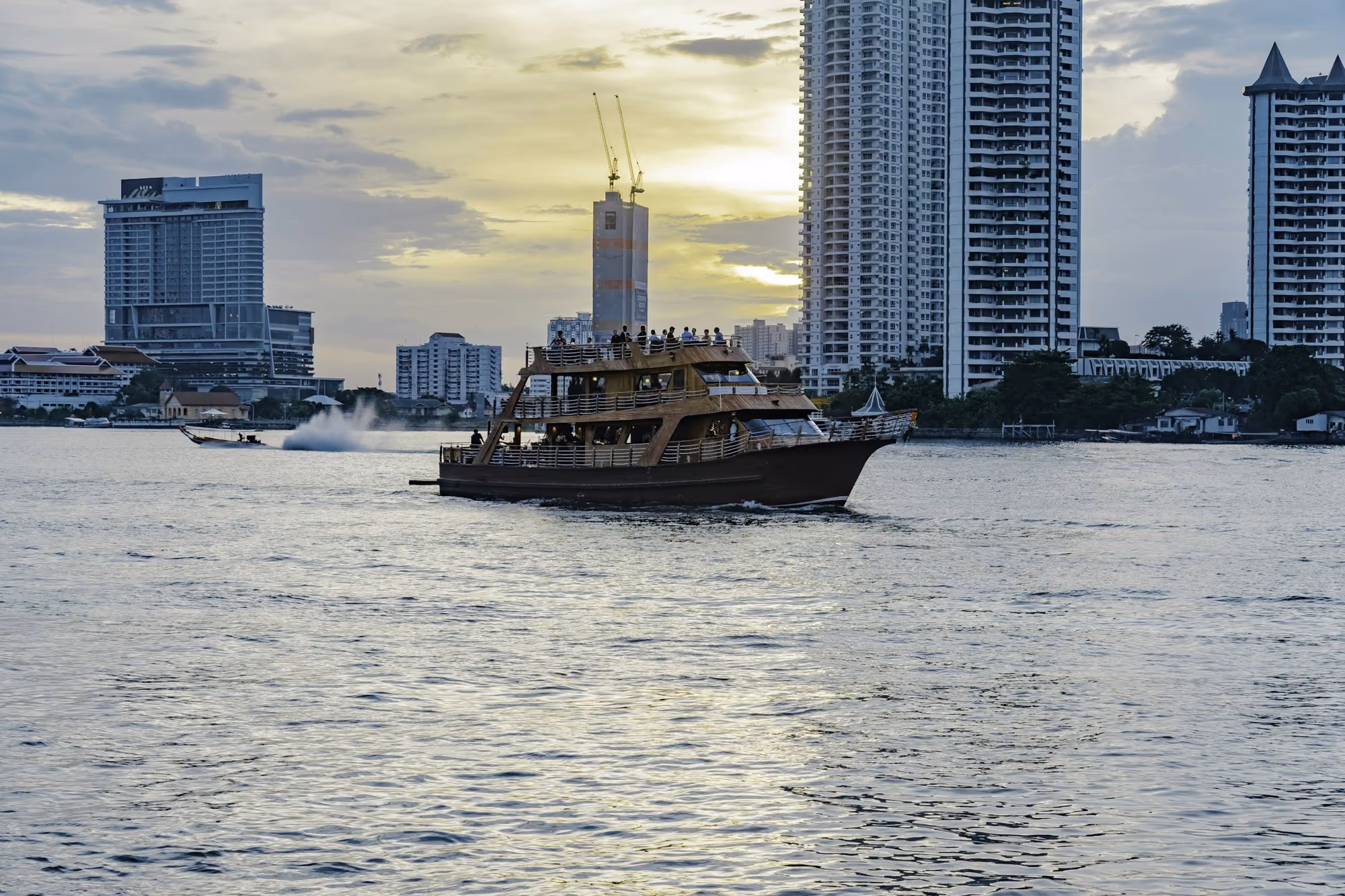 Near Mandarin Oriental Bangkok: a boat traveling through the water in front of tall buildings