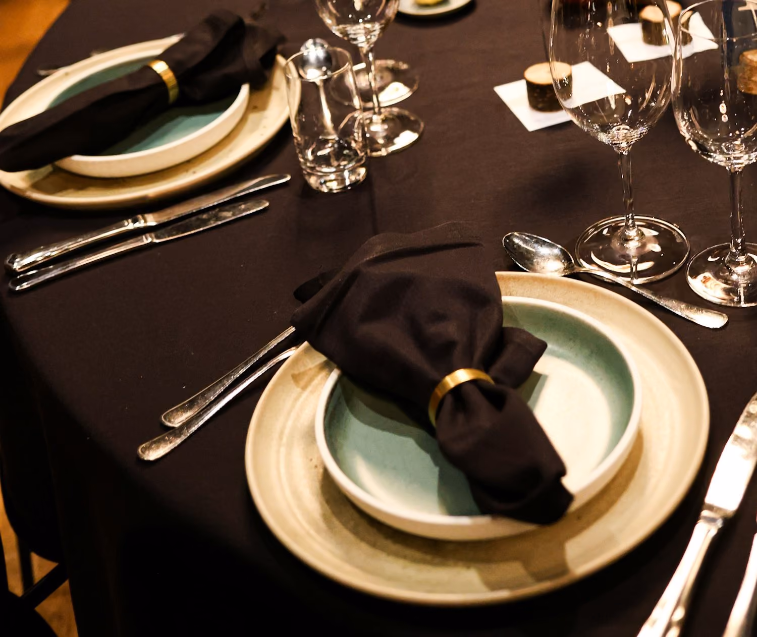 A formal dinner place setting with dark linen, a brass napkin ring and crystal glasses