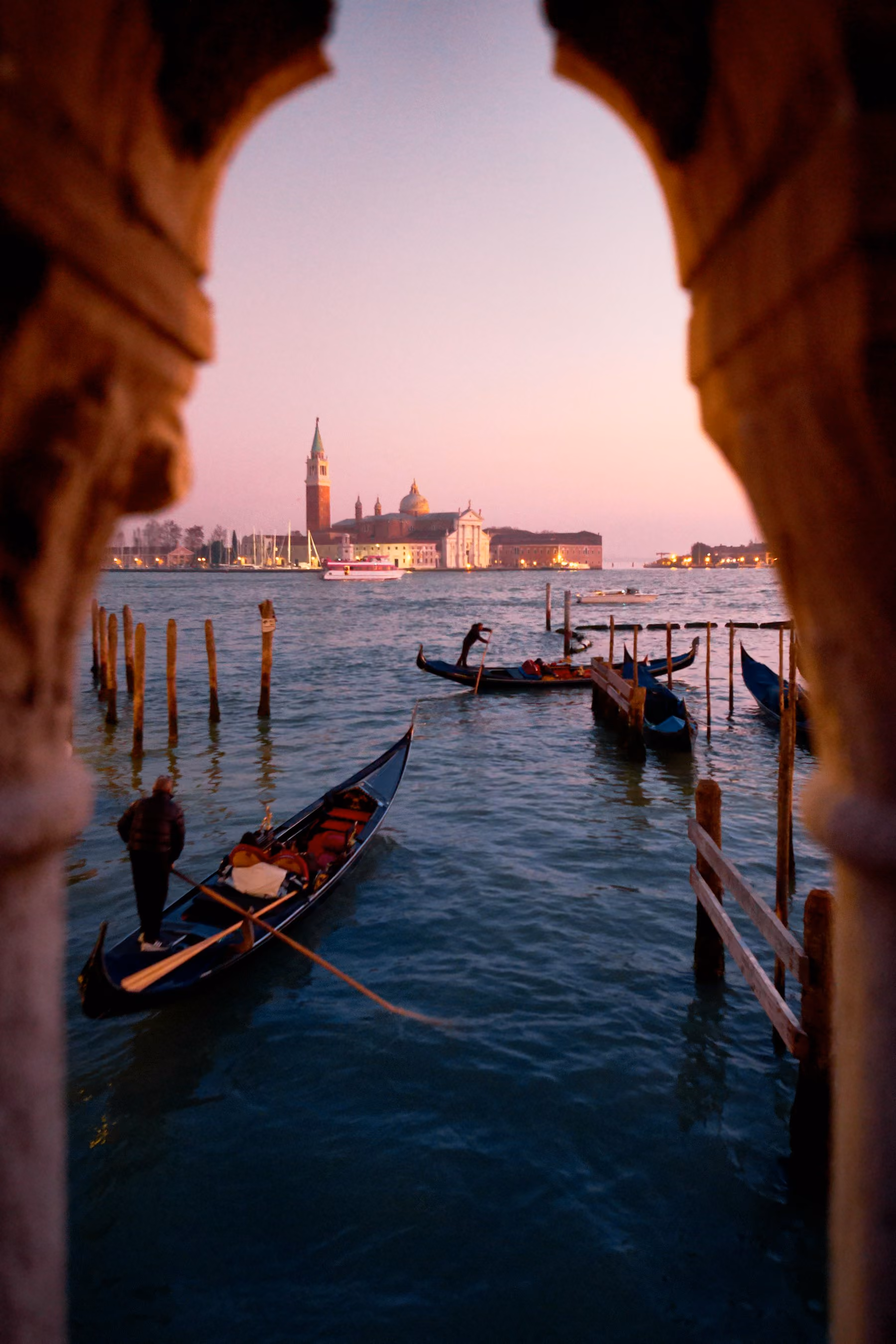 Gondolas moored on the lagoon at dusk, seen through a Venetian arch towards San Giorgio Maggiore
