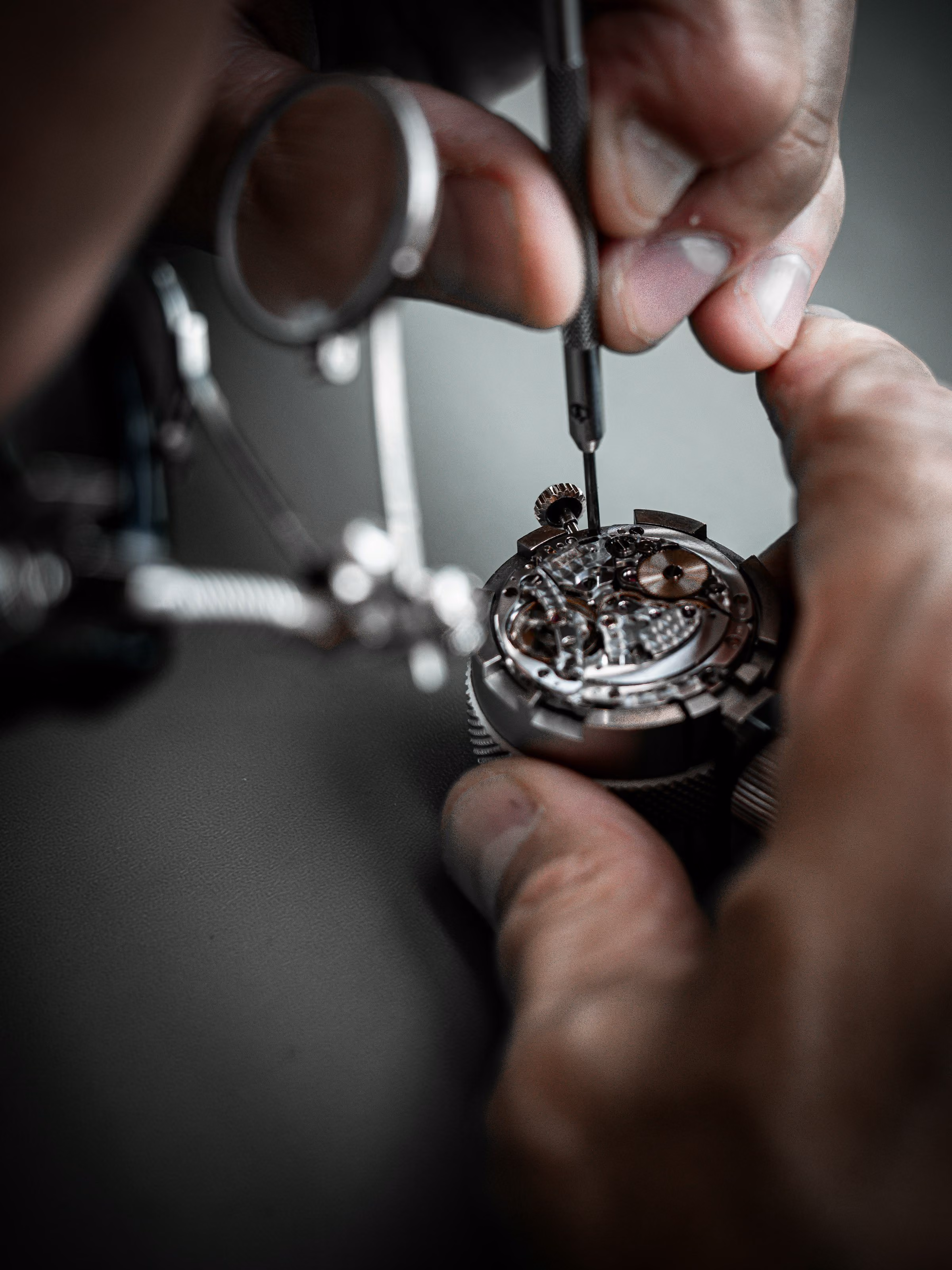 Checking a used watch properly: a watchmaker's hands and tools on an open movement