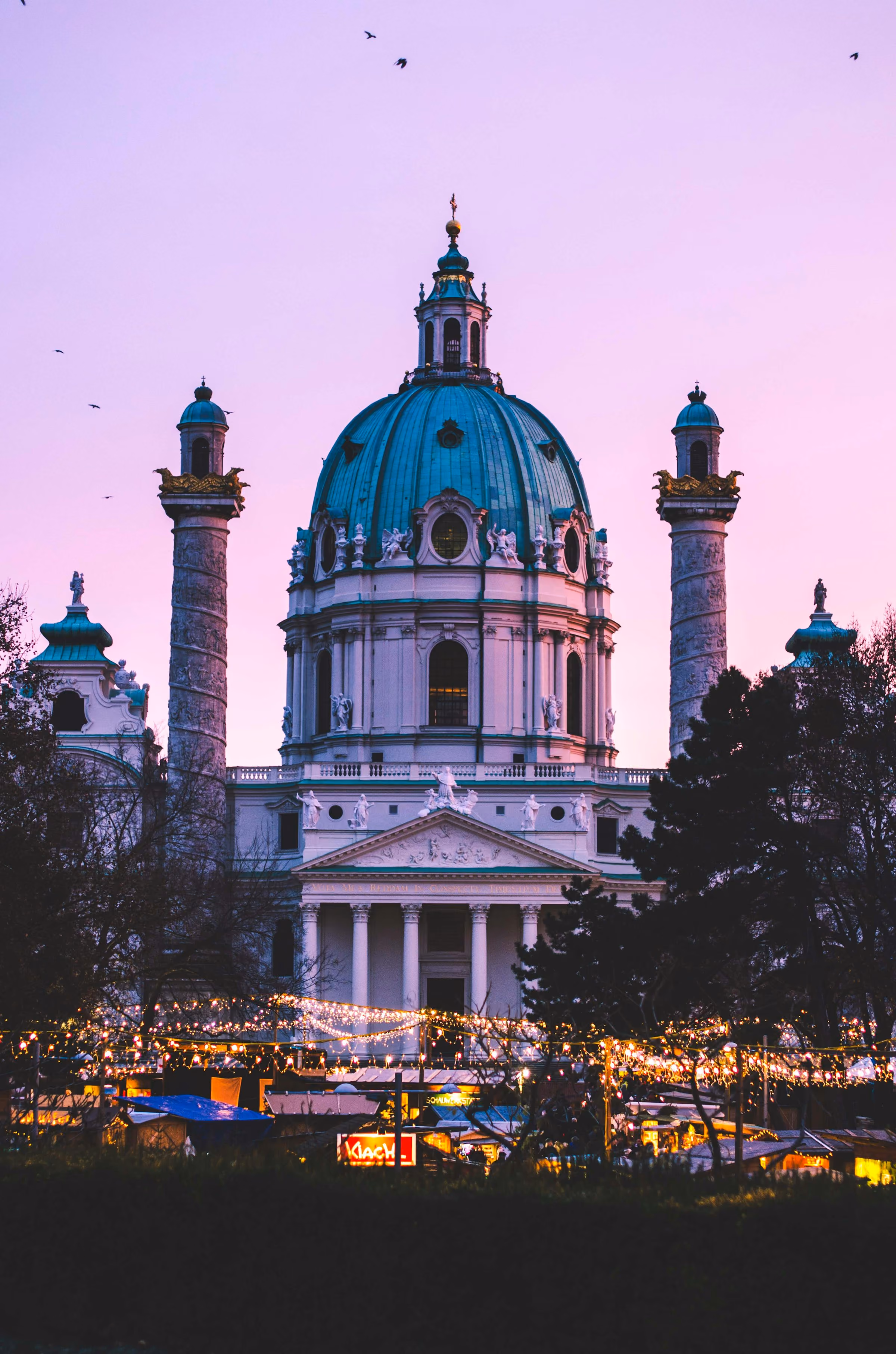 The Karlskirche in Vienna above a lit Christmas market
