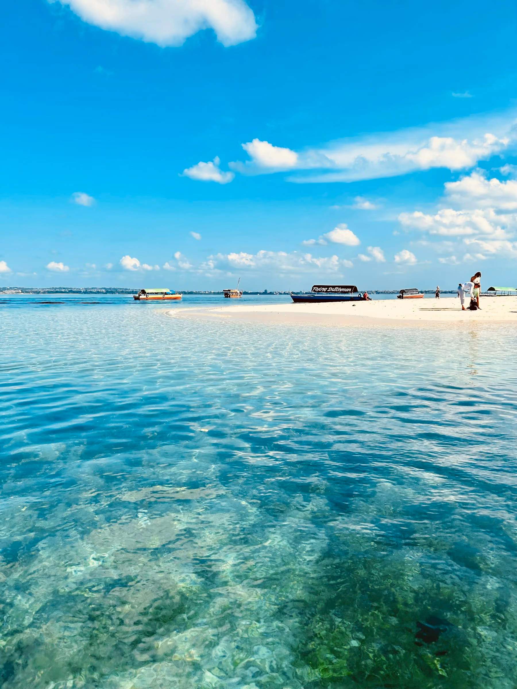 Clear shallow water over white sand and a sandbank off the coast of Zanzibar